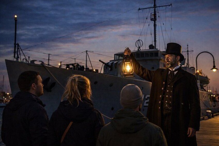 A person holding a lantern, a large ship, and a dock with other ships in the background. 4
