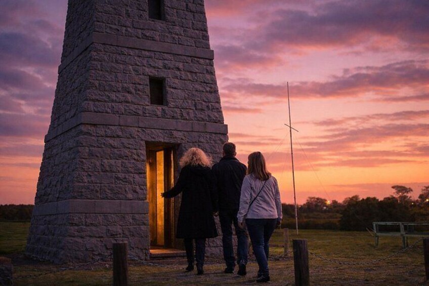 A stone tower with a lit interior, surrounded by a field at sunset. 2