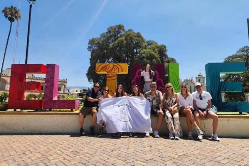 A group of people sitting on a brick-paved area with colorful letter sculptures in the background. 2