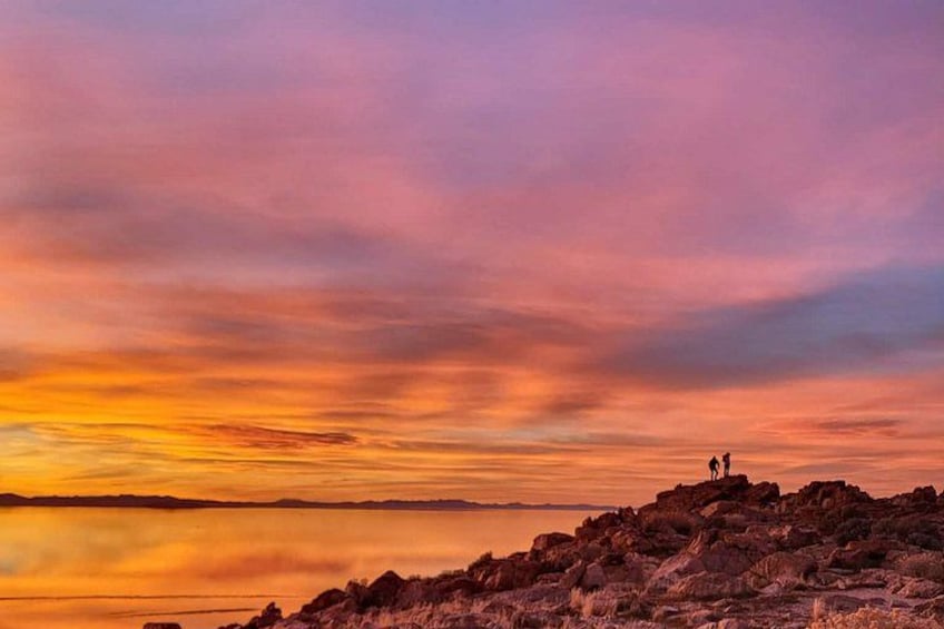 A sunset over a rocky landscape with two figures standing on a hill. 5