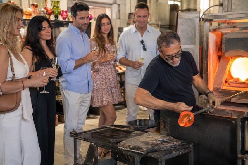A group of people observing a glassblowing process in a workshop. 5