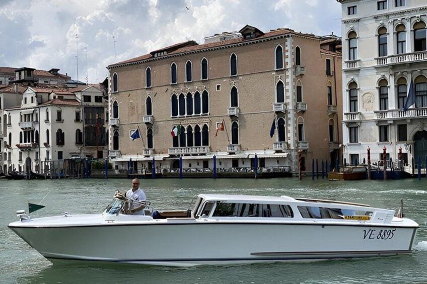 A boat with 'VE 8895' on its side, a man steering it, and buildings with arched windows in the background. 4