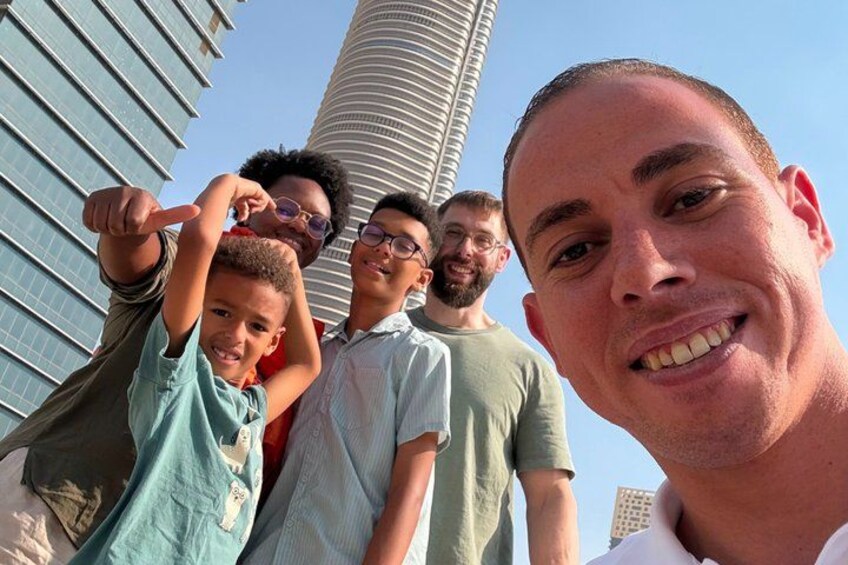 A group of people posing in front of a tall, modern building with a curved facade. 1