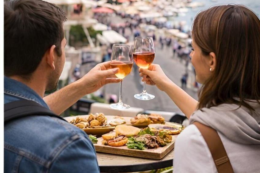 Two people toasting with wine glasses, a plate of food, and a busy street in the background. 1