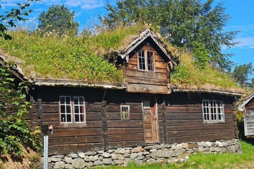 A traditional wooden house with a thatched roof, surrounded by greenery and a stone wall. 3