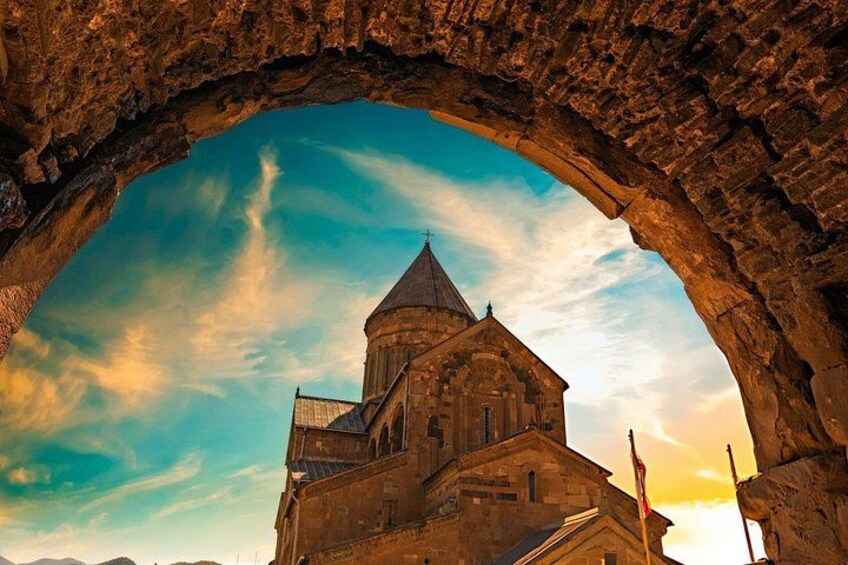 A stone archway framing a building with a dome and a cross, under a clear sky. 3