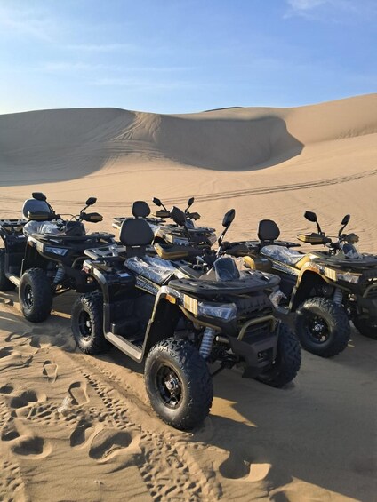 A row of ATVs parked on a sandy desert surface with dunes in the background. 5