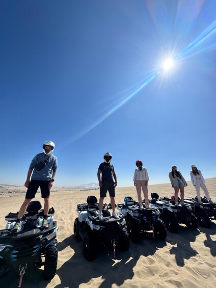 A group of people standing on ATVs in a desert with a clear sky. 4