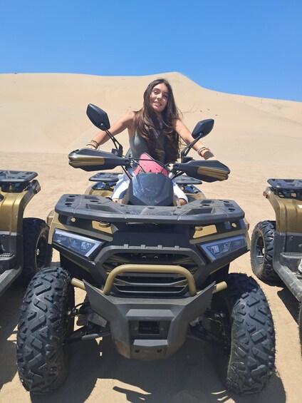 A person on a quad bike in a desert with sand dunes in the background. 3