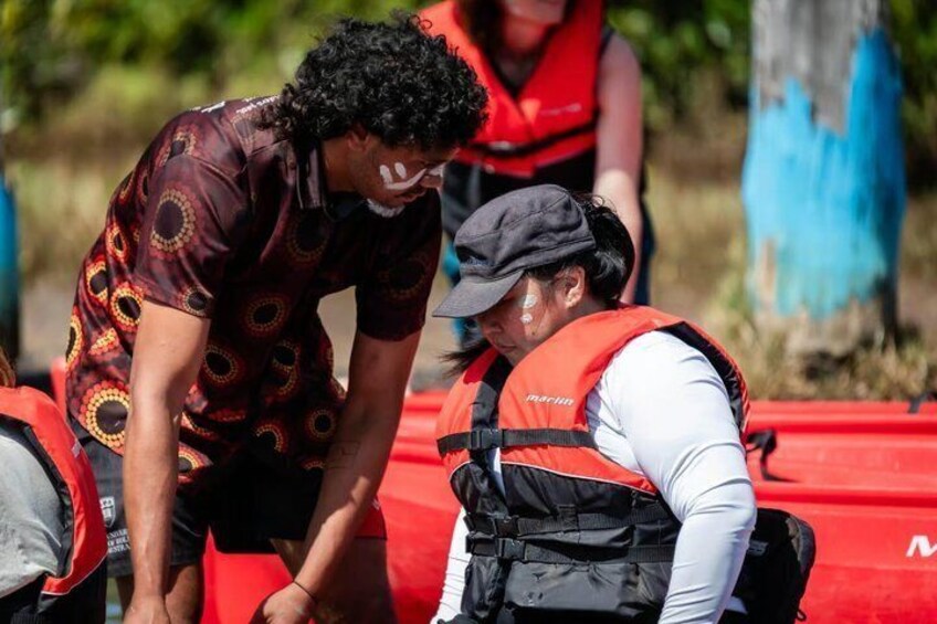 A person in a patterned shirt and another in a life jacket near a red kayak. 3