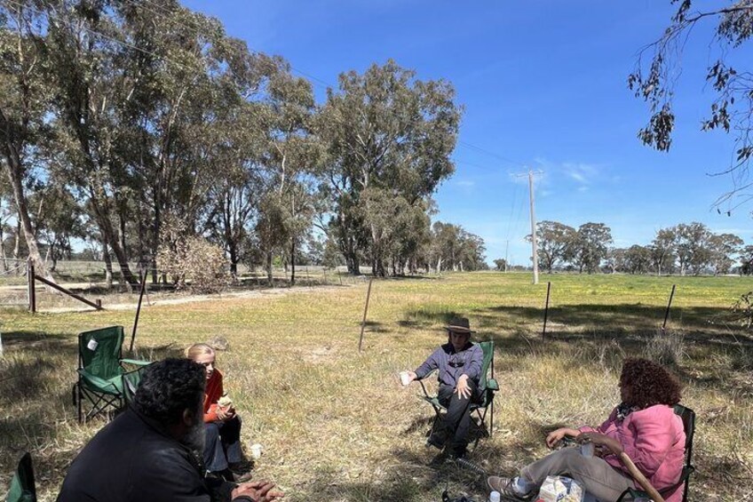 Three people sitting on chairs outdoors, surrounded by trees and grass. 1