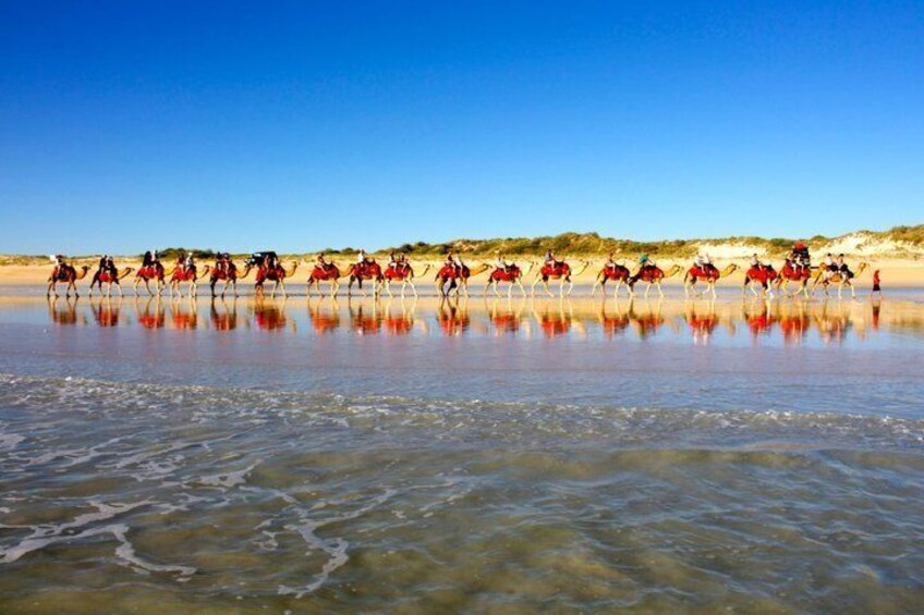 A group of riders on horses crossing a shallow water body with a clear sky. 5