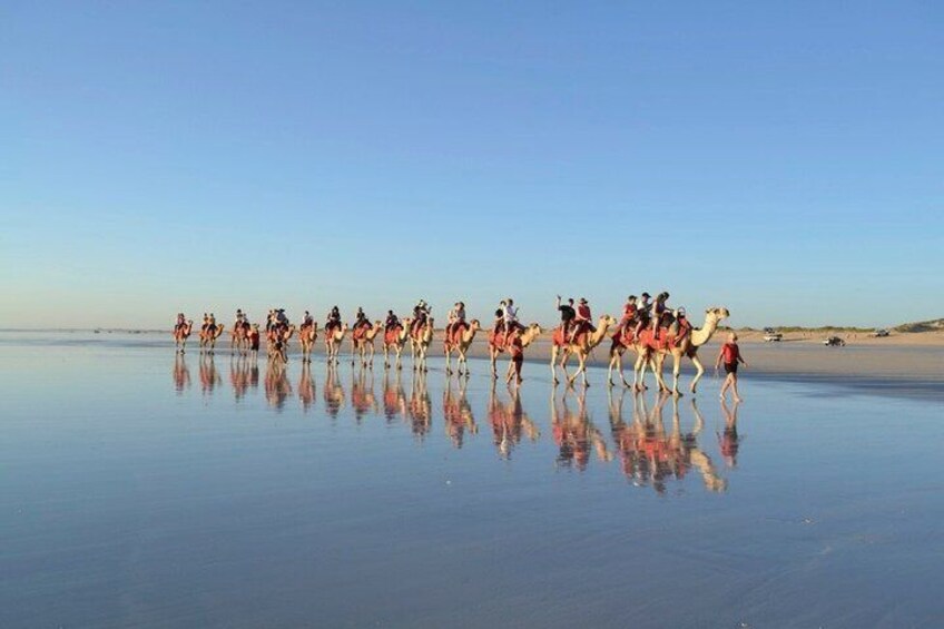 A group of people riding camels on a reflective water surface. 4