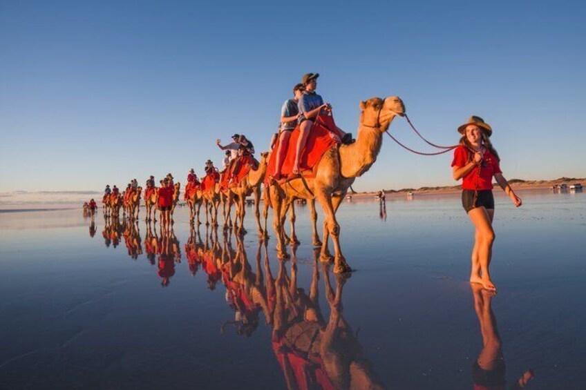A group of people riding camels on a reflective surface, likely salt flats, with a clear sky. 1
