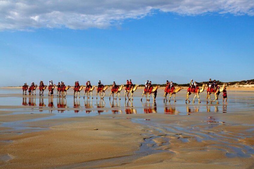 A group of people riding camels on a beach. 3