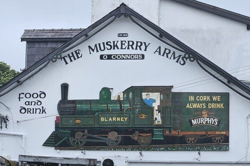 A building with a mural of a green train and the text 'The Muskerry Arms' and 'food and drink'. 2
