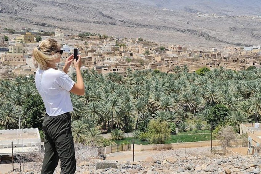A person taking a photo of a town with palm trees and a mountainous backdrop. 3