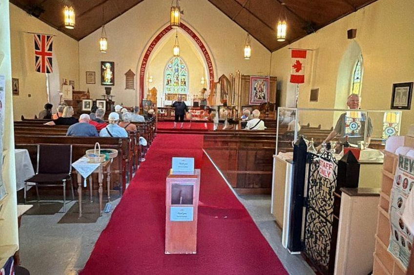 A church interior with pews, a red carpet, a stained glass window, and flags. 4
