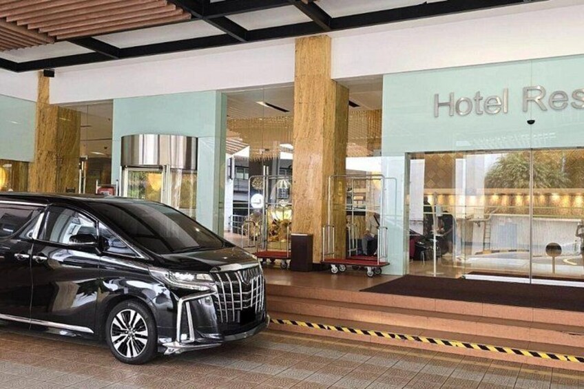 A black van parked in front of a hotel entrance with a luggage cart nearby. 4