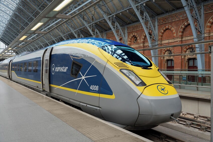 A Eurostar train at a station with a modern roof structure and brick architecture in the background. 1
