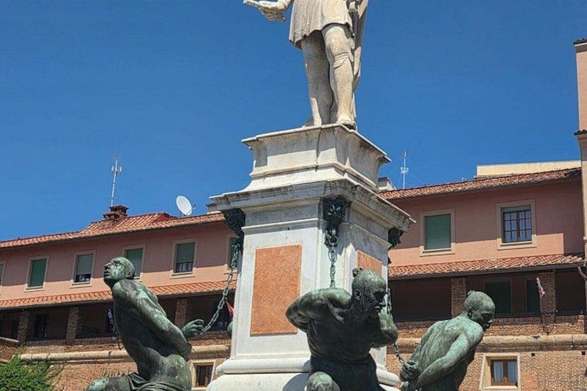 A statue of a man holding a sword, surrounded by three bronze figures, with buildings in the background. 5