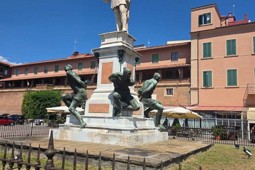 A bronze statue of a man in a dynamic pose, a fountain, and a building with red-tiled roofs in the background. 3