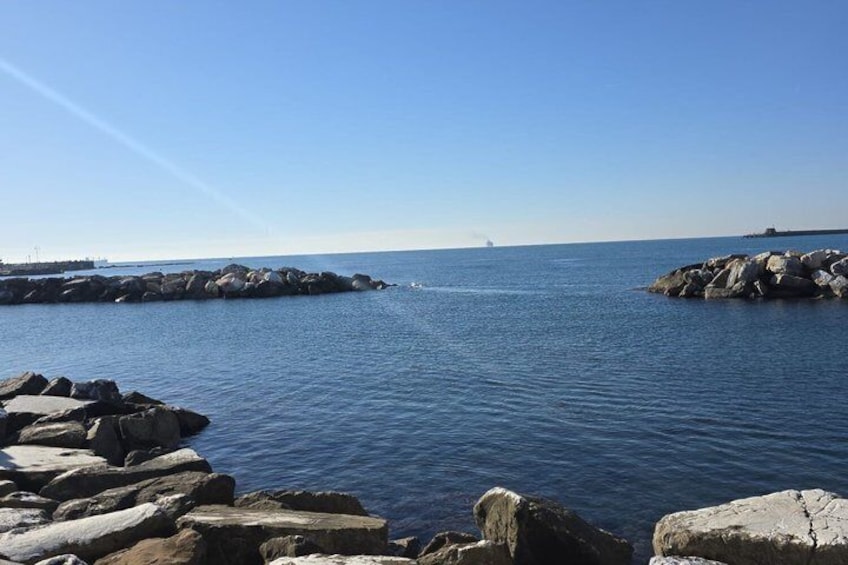 A calm sea with large rocks in the foreground and a distant ship on the horizon. 1