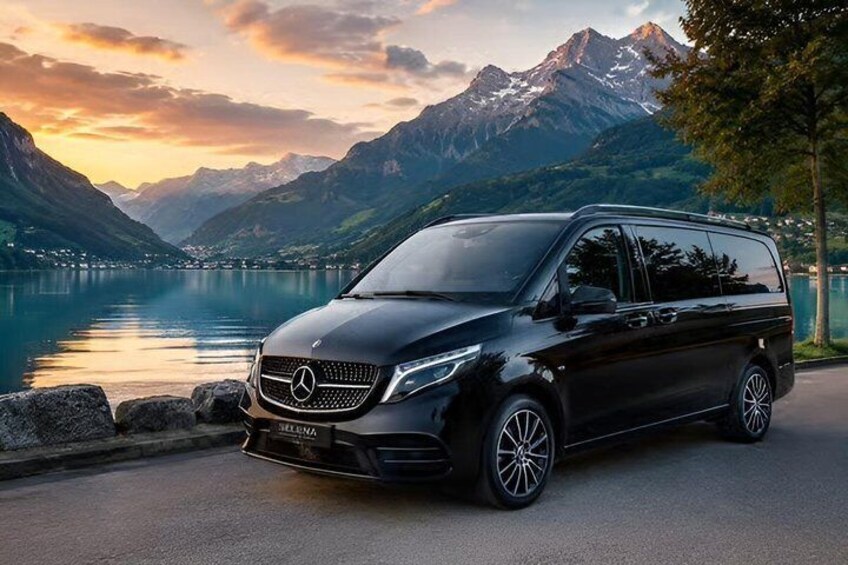 A black Mercedes-Benz Sprinter van parked by a lake with mountains in the background. 2