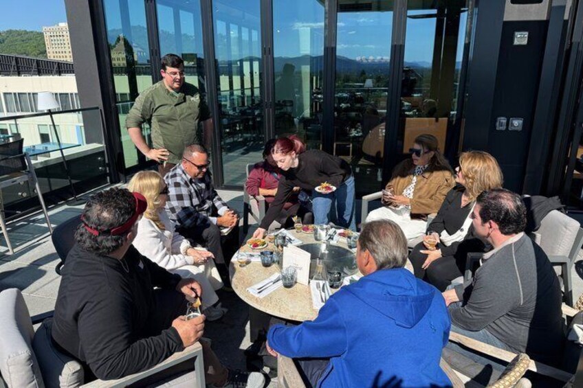 A group of people seated around a table outdoors, engaged in conversation. 4
