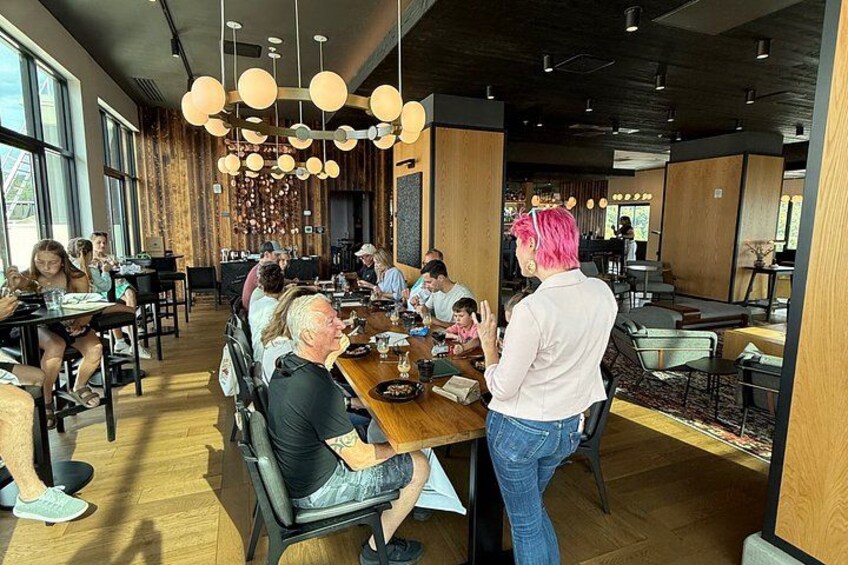 Un interior de restaurante moderno con pisos de madera, lámparas colgantes y un grupo de personas cenando en mesas. 1