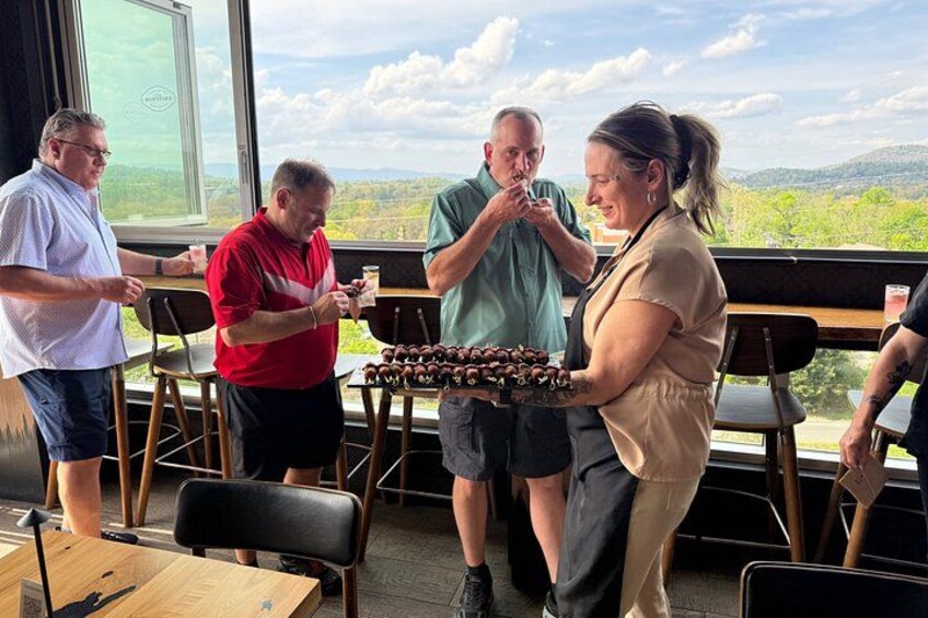 A group of people at a table with a scenic view, holding a tray of food. 2