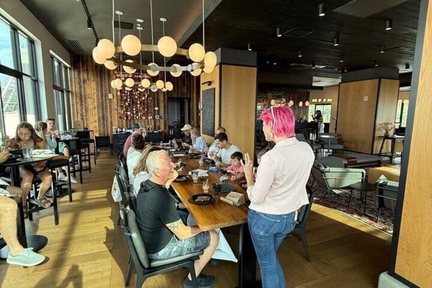 A modern dining area with wooden tables and chairs, large windows, and hanging pendant lights. 1