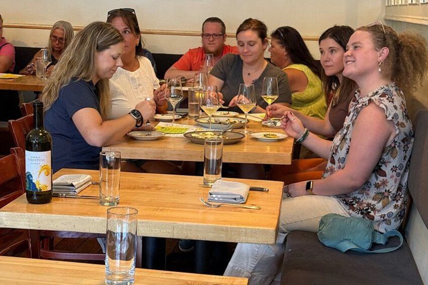 Un grupo de personas cenando en una mesa de madera con copas de vino y platos. 2