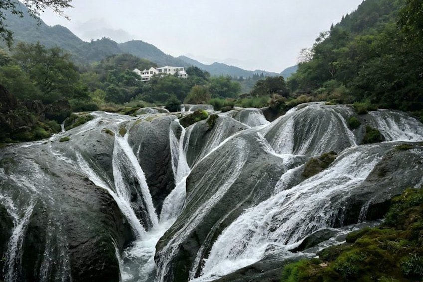 A waterfall cascading over rocks with a house in the background. 3