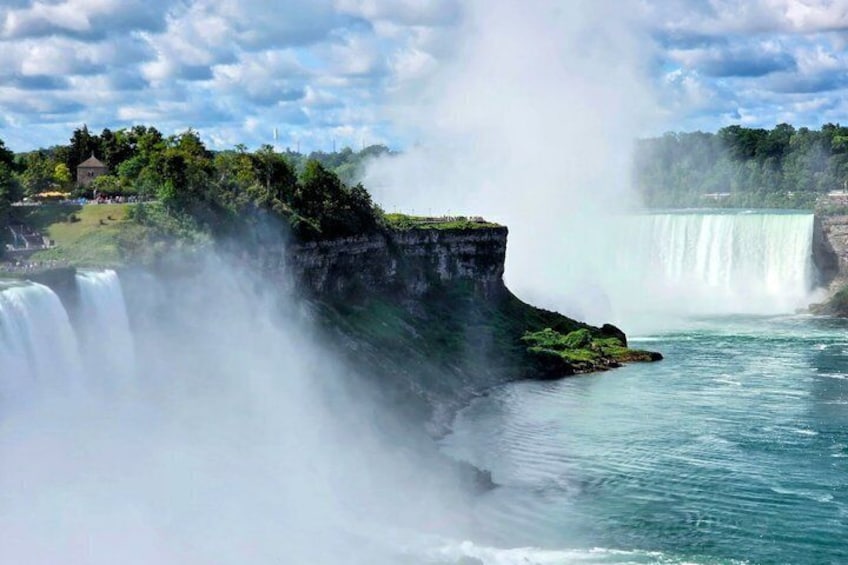 A large waterfall with mist rising from the base, surrounded by greenery and a clear sky. 2
