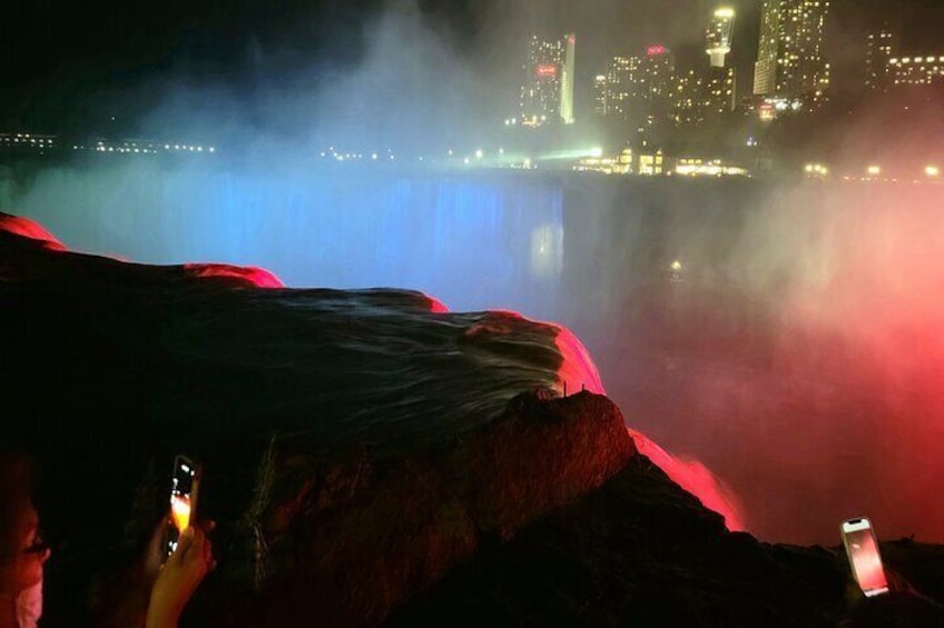 A waterfall with mist, a city skyline in the background, and people taking photos. 4