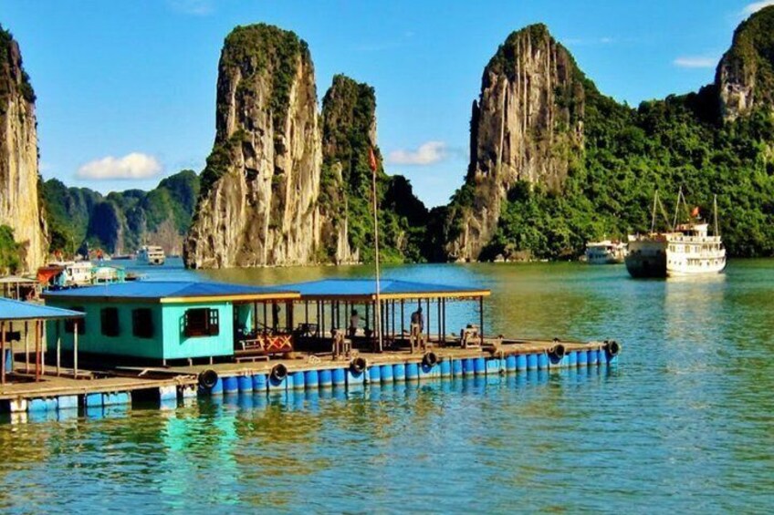 A floating house with a blue roof, surrounded by calm water and tall limestone cliffs. 3