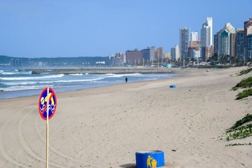 A beach with a lifeguard sign, a blue barrel, and a city skyline in the background. 5
