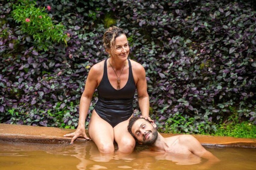 Una persona con traje de baño negro de pie detrás de otra persona recostada en una extensión de agua poco profunda. 2