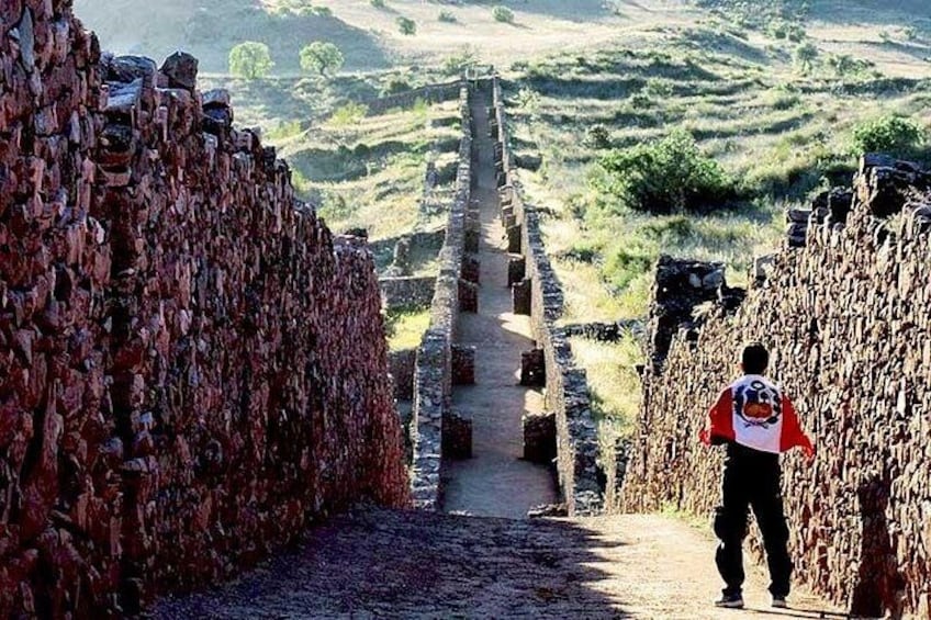 A person walking on a stone pathway surrounded by stone walls. 4