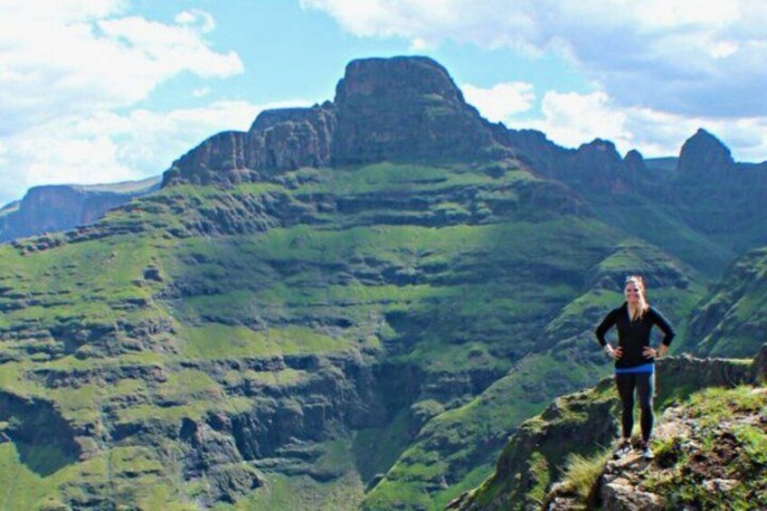 A person standing on a mountain ridge with green valleys and rocky cliffs in the background. 2