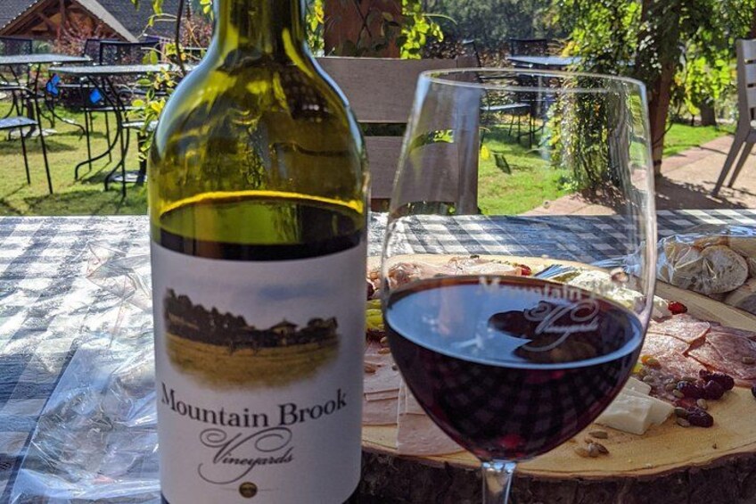 A bottle of Mountain Brook Vineyards wine and a glass of red wine on an outdoor table with a checkered tablecloth. 3