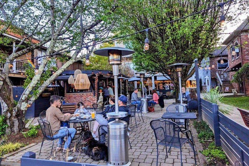 An outdoor café with tables and chairs, surrounded by trees and a brick building. 5