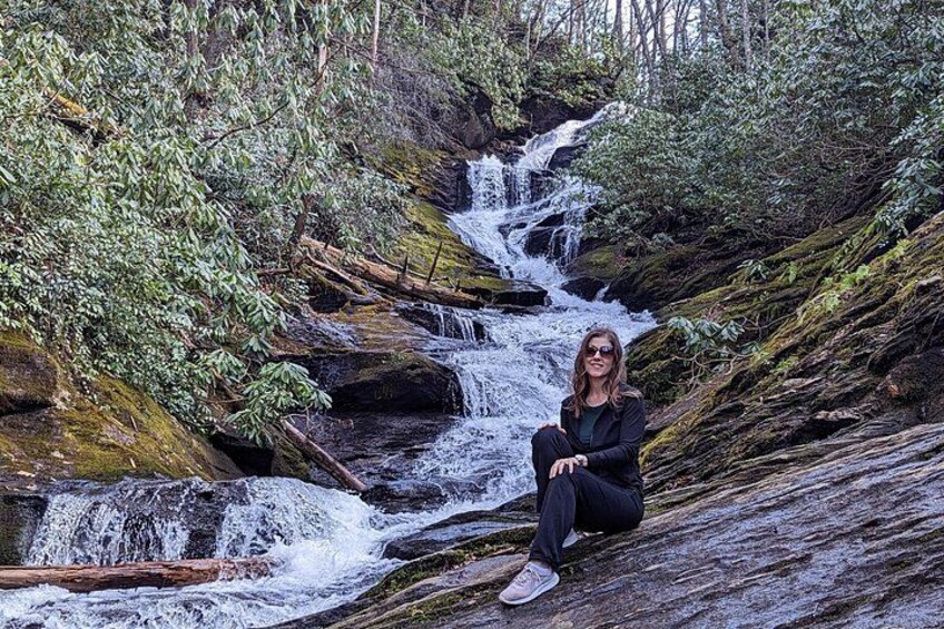A person sitting on a rock by a cascading waterfall in a forested area. 4
