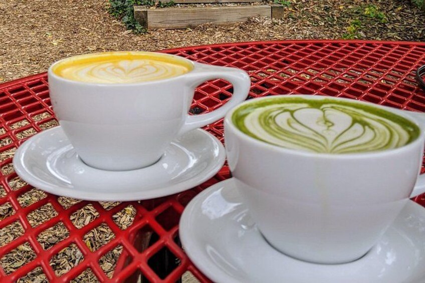 Two white cups of coffee on a red metal table with a lattice pattern. 2