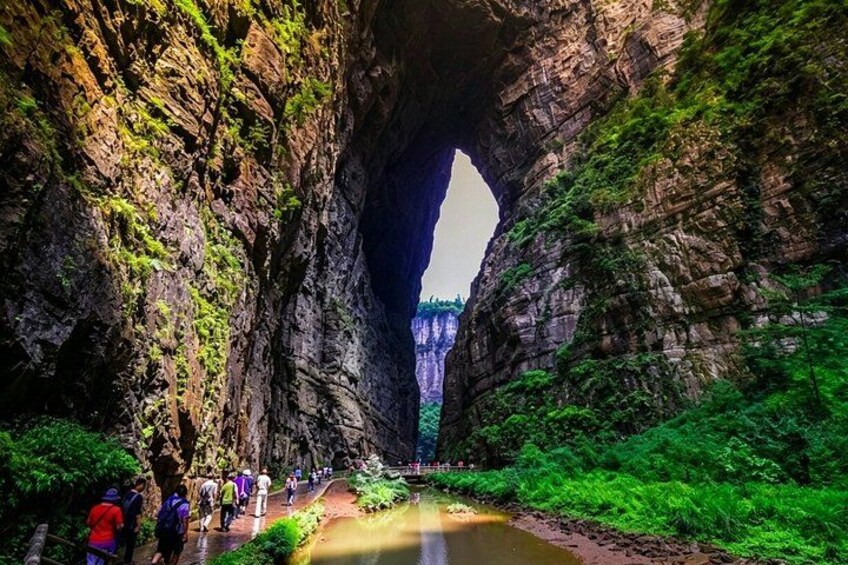 A large rock arch with a river flowing through it, surrounded by lush greenery. 1