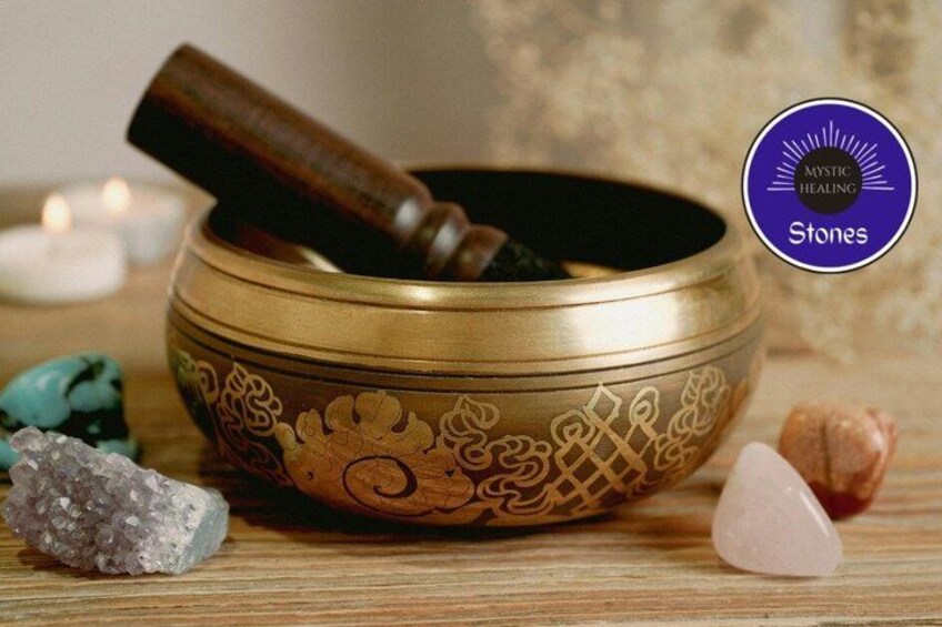 A brass singing bowl with intricate designs, surrounded by various stones and a wooden mallet. 1