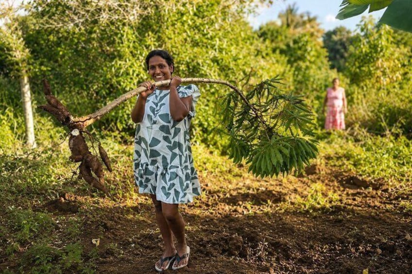 A person in a patterned dress holding a branch, standing in a forested area with a dirt path. 5