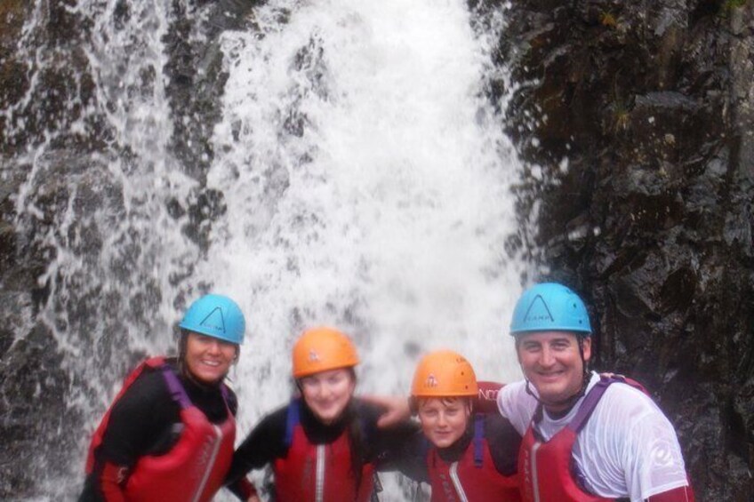 Four people wearing helmets and life jackets standing in front of a waterfall. 4