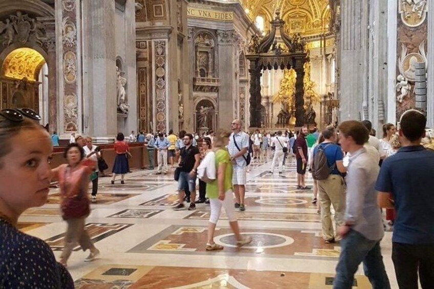 A crowded interior of a grand building with ornate columns and a large central altar. 5